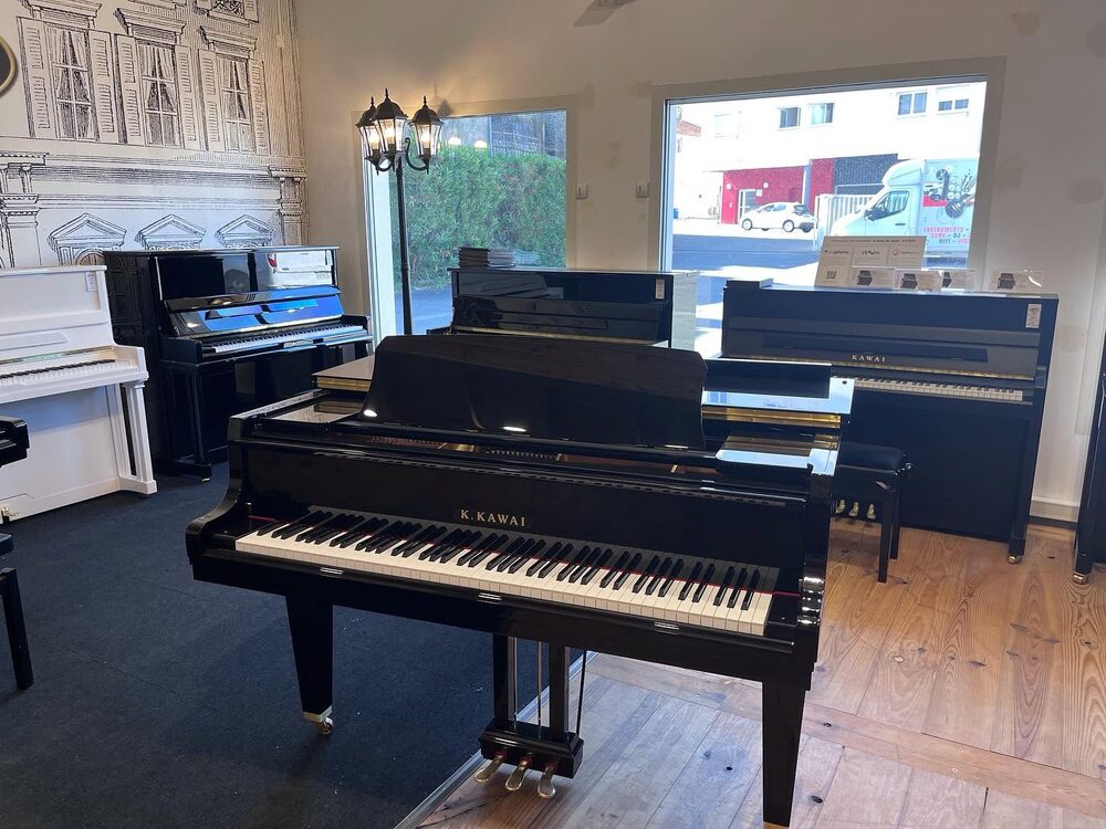 Piano à queue Kawai exposé devant des pianos droits, magasin Ubico Musique à Dax